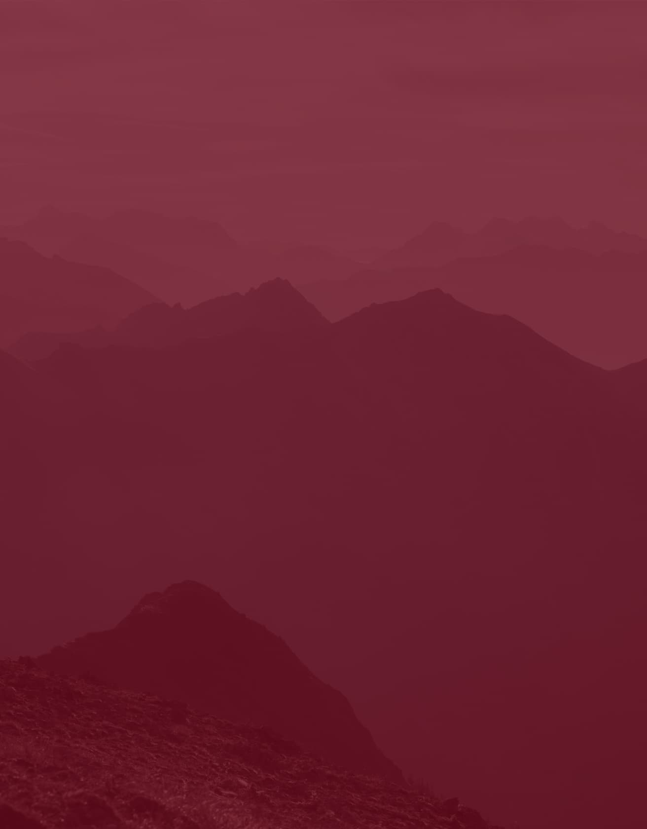 Silhouettes of mountain peaks under a red hue.
